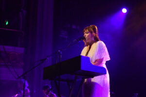 Angel Olsen at a piano bathed in purple stage light.