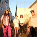 Four members of Sutros standing outside in the bright sun between buildings